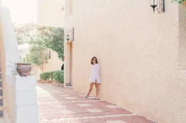 Beyaz elbiseli genç bir kadın gün batımında eski şehir sokağında yürüyor..