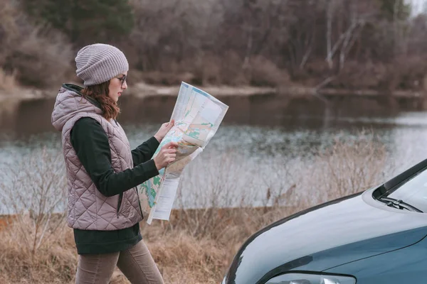 Joven mujer está sosteniendo y viendo hoja de ruta cerca de coche . —  Fotos de Stock