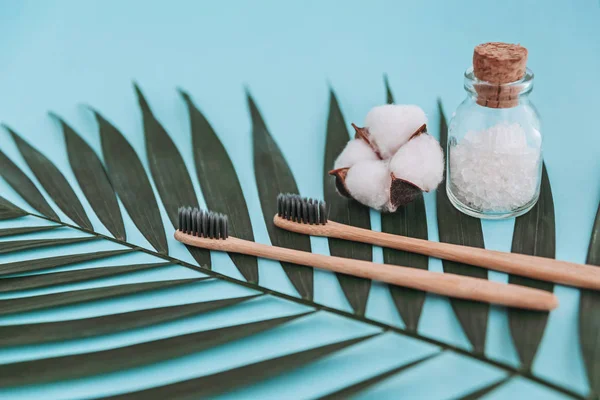 Bambuszahnbürsten, Glasflasche mit Meersalz, Baumwollblume auf Palmblatt auf blauem Hintergrund. Null-Abfall-Konzept. — Stockfoto