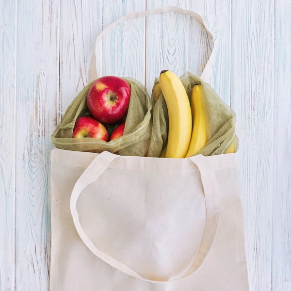 Worek wielokrotnego użytku z jabłkami i bananami na białym tle drewnianym. Koncepcja darmowych zakupów bez odpadów i tworzyw sztucznych. — Zdjęcie stockowe