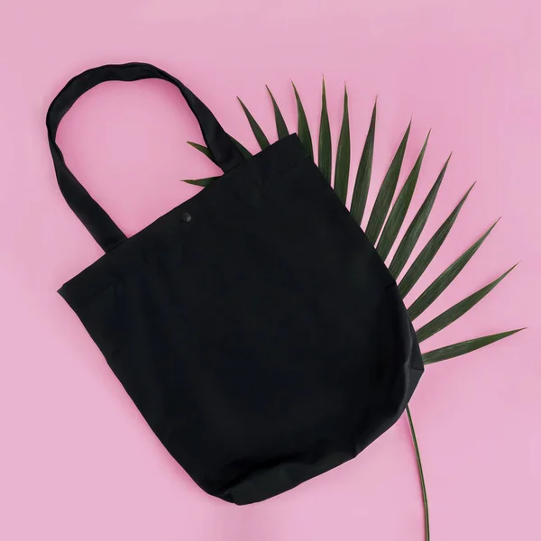 Black cotton bag and palm leaf on pink background. Mock up for design.