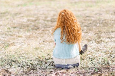 Beyaz elbiseli ve mavi kazak lı romantik genç kadın, ilkbahar çiçek açan bahçede yerde oturuyor. Geri görünüm.