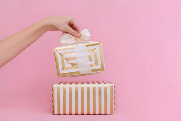 Manos de mujer sosteniendo regalo o caja de regalo sobre fondo pastel rosa . — Foto de Stock