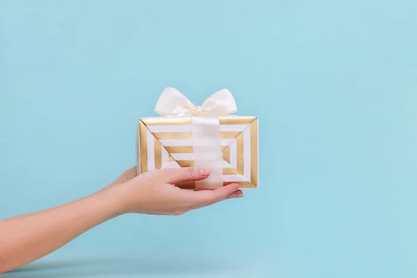 Manos de mujer sosteniendo regalo o caja presente sobre fondo pastel azul . — Foto de Stock