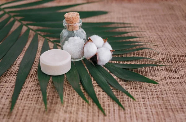 Seife, Meersalz in Glasflasche und Baumwollblume auf Palmblatt Hintergrund. — Stockfoto