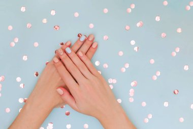 Kopya alanı ve konfeti ile mavi arka plan üzerinde pastel manikür ile Kadın elleri.