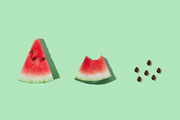 Slice of ripe watermelon and seeds on mint green background. Process of eating watermelon from whole slice to seeds. — Stock Photo, Image