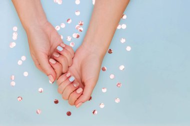 Mavi arka planda pastel manikürlü kadın elleri. Fotokopi alanı ve altın konfeti..