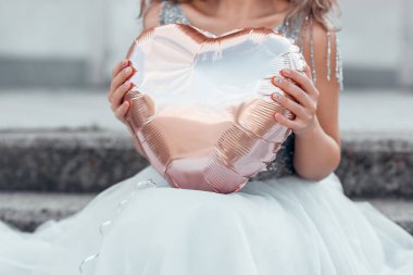 Elinde pembe altın bir kalp taşıyan güzel elbiseli bir kadın..