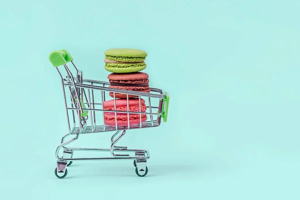 Surtido de macarrones coloridos en el carrito de la compra de juguetes en fondo verde menta con espacio de copia . —  Fotos de Stock