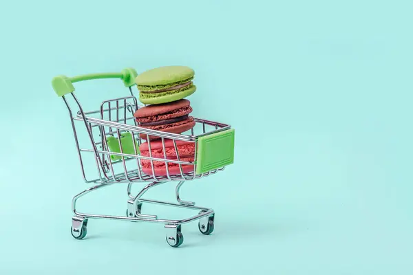 Surtido de macarrones coloridos en el carrito de la compra de juguetes en fondo verde menta con espacio de copia . — Foto de Stock