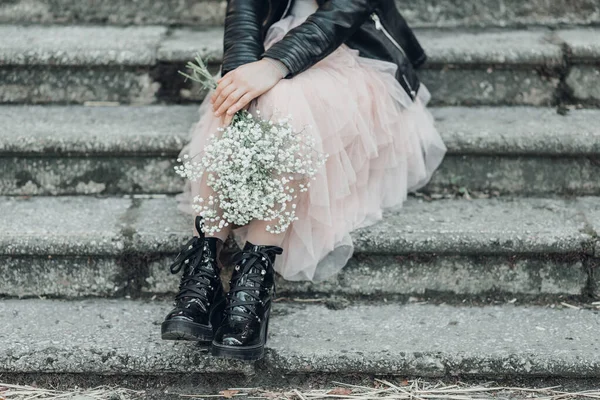 Woman in pink lace skirt with white flowers bouquet in her hands is sitting on stairs.