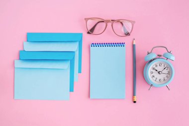 Mavi mektup zarfları, pembe arkaplanlı saat ve defter fotokopi alanı. Okula dönmek ya da iş kavramı. Üst görünüm.