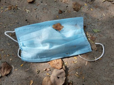 Tek kullanımlık mavi yüz maskesi şehir yolu şeridinde bir yere atılmış. Covid-19 (koronavirüs) salgını sırasında çevresel kirlilik ve atık.