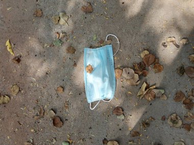 Tek kullanımlık mavi yüz maskesi şehir yolu şeridinde bir yere atılmış. Covid-19 (koronavirüs) salgını sırasında çevresel kirlilik ve atık.