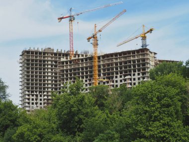Çok katlı binaların inşaatı. Konut ve İnşaat vinçleri gökyüzü arka plan üzerinde. Binaların önünde yeşil ağaçlar