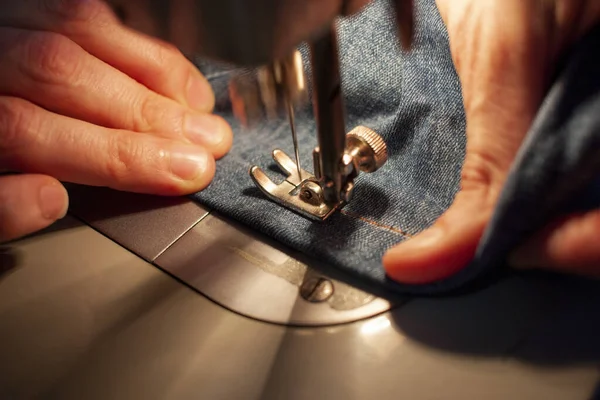 Женские руки на старой швейной машинке, которая шила джинсы. Крупный план — стоковое фото