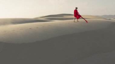 Çölde kum tepelerinin zirvesinde yürüyen bir kızın 4K hava görüntüsü.