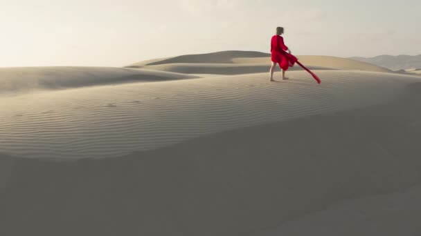 Çölde kum tepelerinin zirvesinde yürüyen bir kızın 4K hava görüntüsü. — Stok video