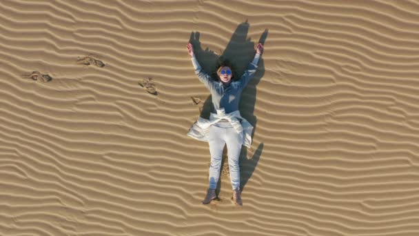 Беспилотник 4К крупным планом видит женщину, отдыхающую на песчаной дюне в пустынной природе — стоковое видео