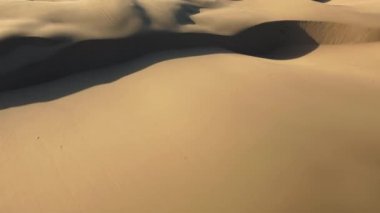 4K hava aracı, gün batımında dalgalı kum tepelerinin tepesinde uçuyor.