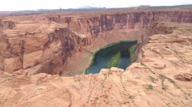 Horseshoe Bend Kanyonu 'nun dalgalı kırmızı uçurumlarında uçan İHA, 4K sinemasal