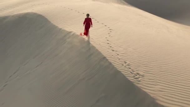 Vista aérea 4K de la mujer caminando por el pico de la duna de arena al atardecer — Vídeos de Stock