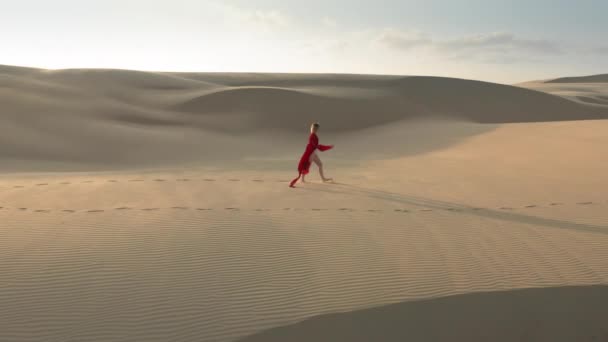 4К вид с воздуха на девушку, идущую по вершине песчаных дюн в пустыне природы — стоковое видео