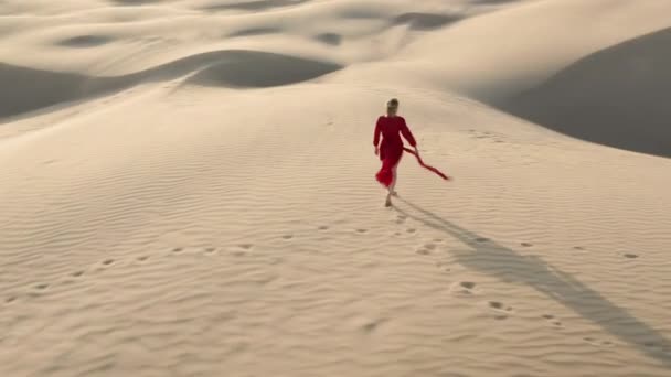 4К вид с воздуха на женщину, идущую по вершине песчаной дюны на закате — стоковое видео