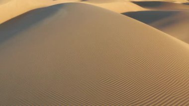 4K hava aracı altın gün batımı ışığında sihirli kum tepeleri üzerinde uçuyor.