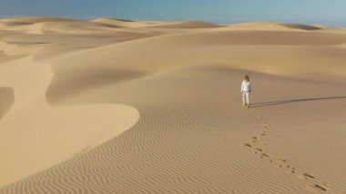 Doğa yolculuğu 4K hava videosu. Genç bir kadın kum tepelerinde yürüyor.