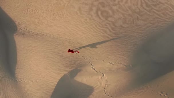 Ludzie strzelali. 4K widok z lotu ptaka kobiety przechodzącej przez wydmy o zachodzie słońca — Wideo stockowe