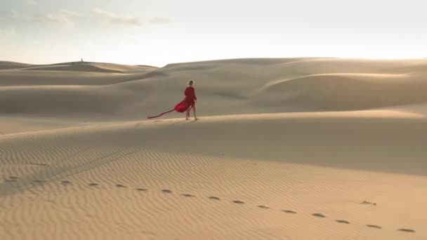 4K vue aérienne d'une fille marchant vers le coucher du soleil avec des dunes de sable paysage
