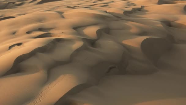 4K hava aracı görüntüsü altın gün batımında dalgalı kum tepelerinin üzerinde uçuyor. — Stok video
