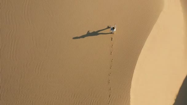 4K aerial view of a girl running by sand dunes in the desert nature, at sunrise — Stock Video