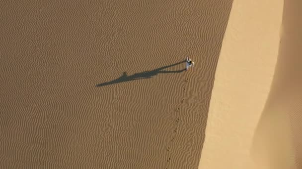 Vista aérea 4K de una mujer caminando por dunas de arena en la naturaleza del desierto, al amanecer — Vídeo de stock