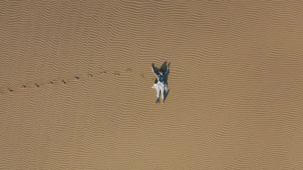 Drone 4K voando para longe da jovem relaxante na duna de areia na natureza do deserto — Vídeo de Stock
