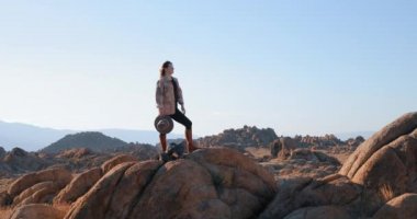 Genç, bağımsız bir kadın, kayalık bir tepede güneşin doğuşunu seyrediyor.