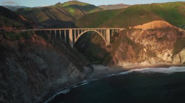 Gün batımı açık havada. İHA, Big Sur parkındaki manzaralı kemer köprüsüne doğru uçuyor.