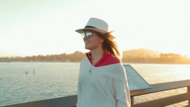 Glückliche attraktive Frau, die an der Seebrücke vorbeiläuft und den sommerlichen Sonnenuntergang mit Wasserblick genießt — Stockvideo