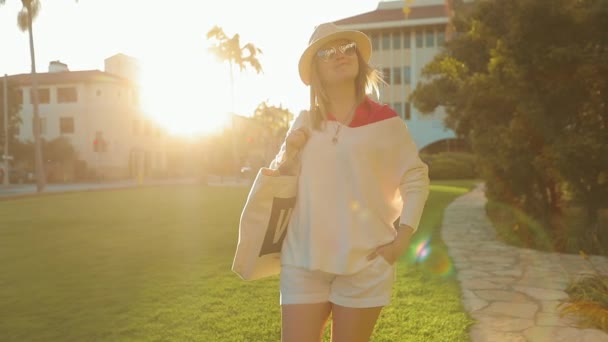 SLOW MOTION: Jovem mulher sorridente em roupa casual andando em luz dourada do pôr do sol — Vídeo de Stock