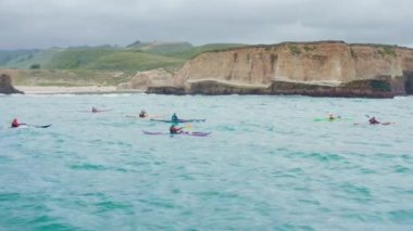 Okyanusta kayak yapan turistler, arka planda yeşil dağlar, 4K