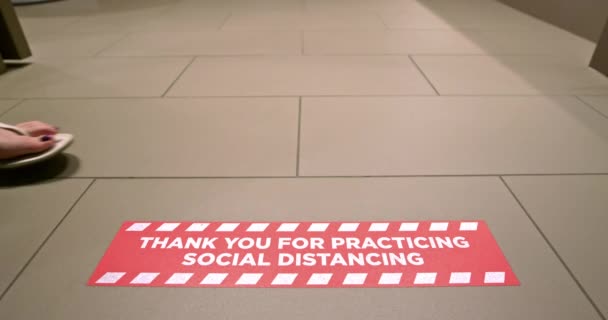 Kvinna promenader längs röda golvet skylt på hotellet som påminner om att träna socialt avstånd — Stockvideo