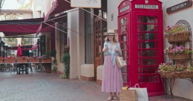 Neşeli gülümseyen kadın kırmızı telefon kulübesinde eğleniyor ve selfie çekiyor.