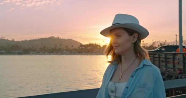 Aantrekkelijke jonge vrouw wandelen door pier met filmische roze zonsondergang op de achtergrond — Stockvideo