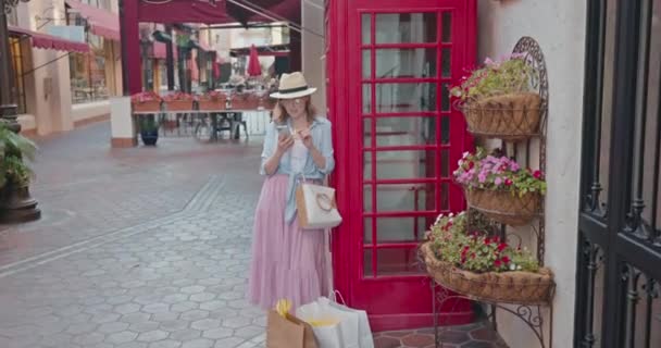 Elegante mujer bonita que comprueba el teléfono inteligente en la cabina telefónica roja de Londres, 4K — Vídeo de stock