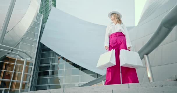 Жінка в стильному одязі з білими сумками позує в торговому центрі, 4K — стокове відео
