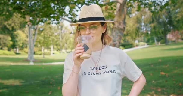 Mooie vrouw is genieten van ijskoffie drinken in het groene park tijdens de lunch — Stockvideo