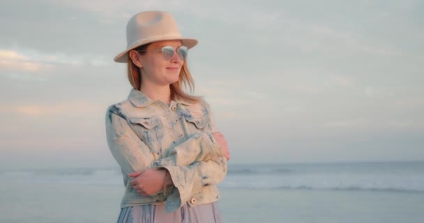 O femeie tânără se simte fericită și inspirată în timp ce contemplă apusul soarelui deasupra oceanului — Videoclip de stoc