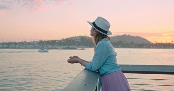 Retrato de cerca de una mujer sonriente disfrutando de la hermosa puesta de sol de oro rosa en el océano — Vídeo de stock